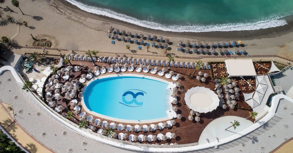 Aerial view of Ocean Club Marbella's oval pool surrounded by white sunbeds beside the beach