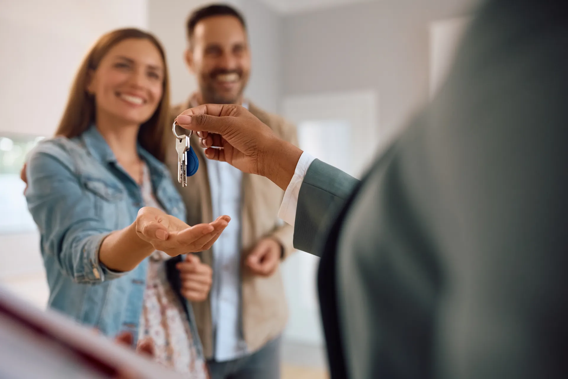 Agent handing over house keys to a smiling couple in a bright empty apartment