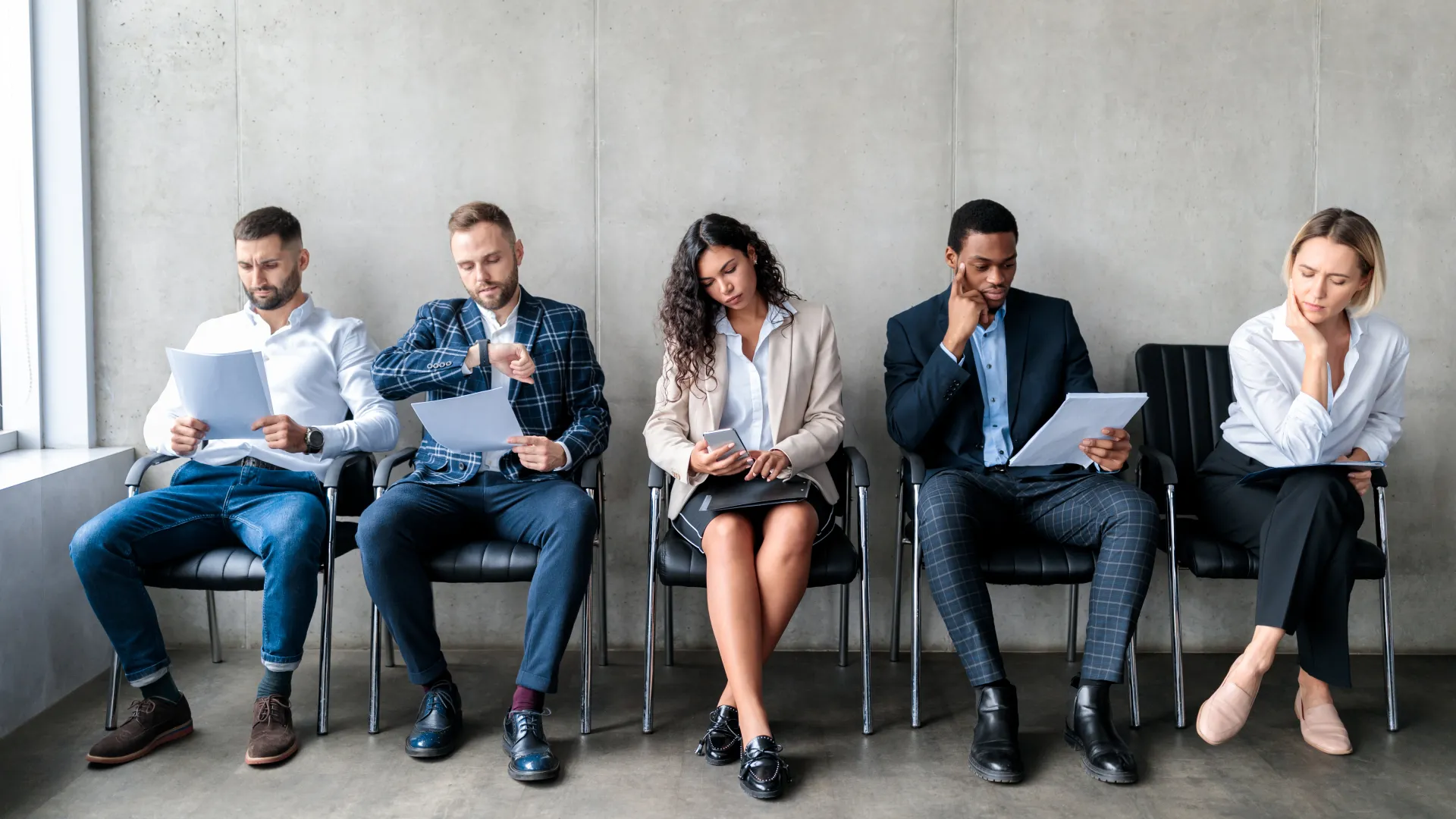 Five job candidates holding resumes while waiting in a row of chairs