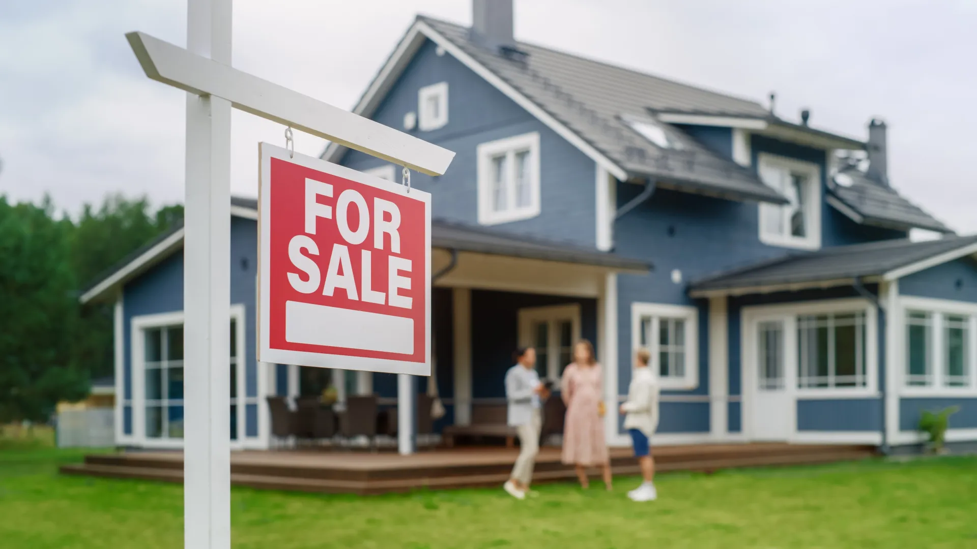 For sale sign in front of a house where an agent talks with a couple