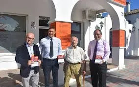 Four men holding orange brochures outside a whitewashed office with orange signage