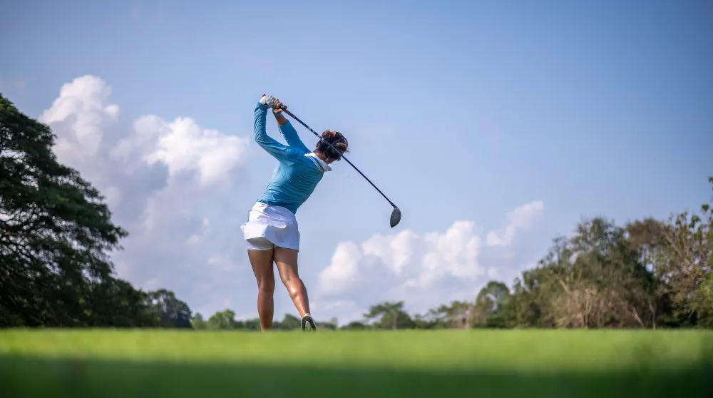 Golfer following through a tee shot on a lush fairway under blue skies