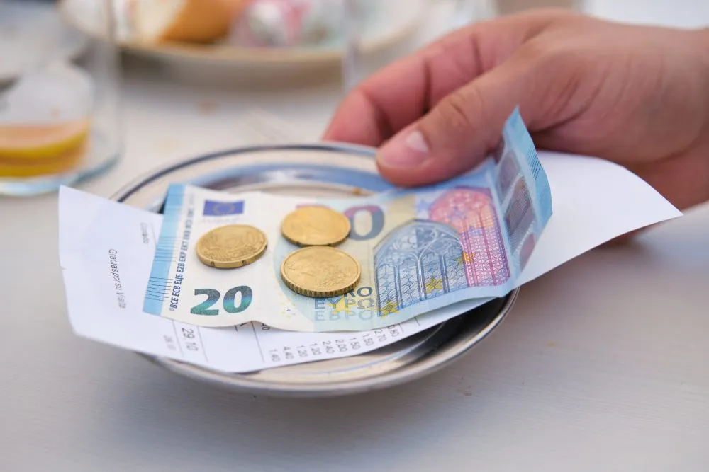 Une main d&eacute;posant des billets et des pi&egrave;ces en euros sur une petite assiette avec l'addition d'un restaurant