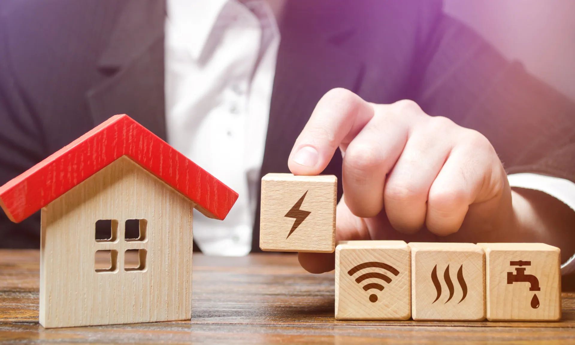 Ręcznie ułożone drewniane klocki z ikonami prądu, Wi-Fi, ogrzewania i wody obok makiety domu