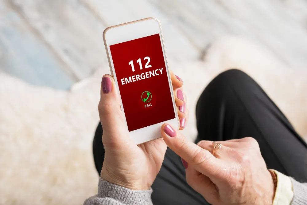 H&auml;nde, die ein Smartphone halten, auf dessen Bildschirm der Notruf 112 angezeigt wird