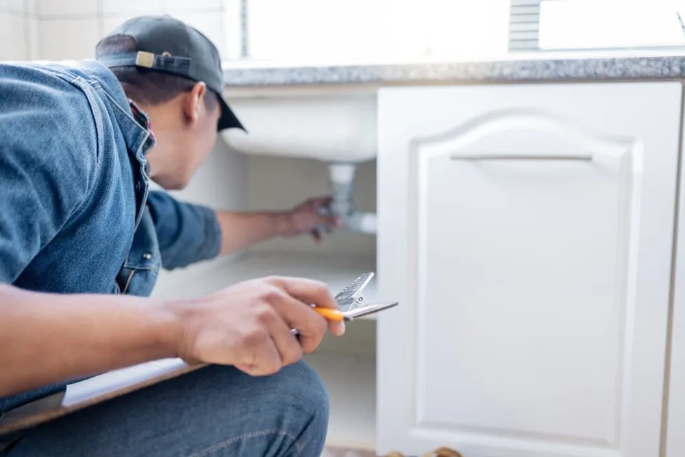 Een inspecteur met een klembord die het sanitair onder een gootsteen controleert