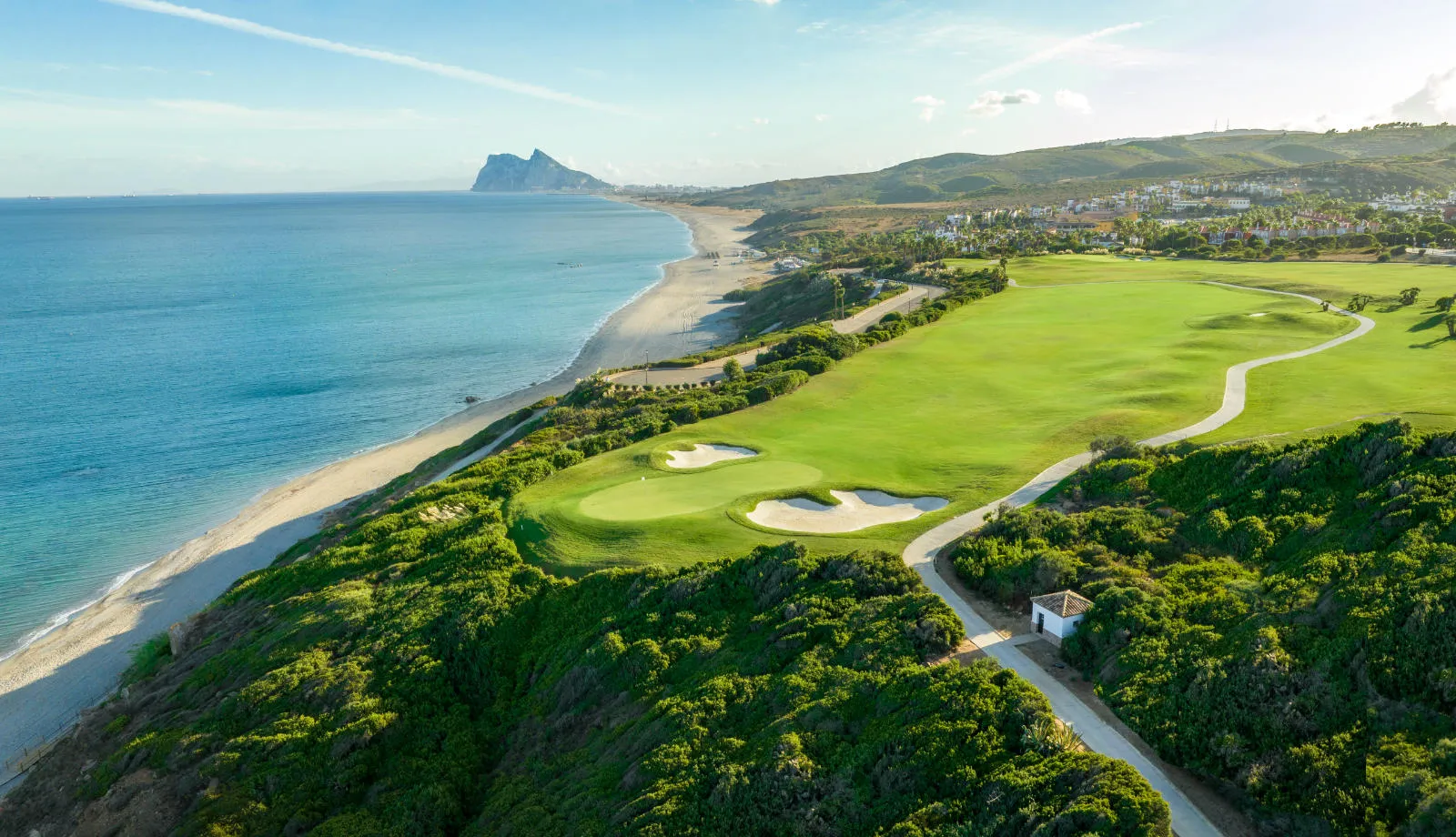 Link do pola golfowego położonego na zielonych klifach nad plażą w Alcaidesa, z Skałą Gibraltarską w oddali