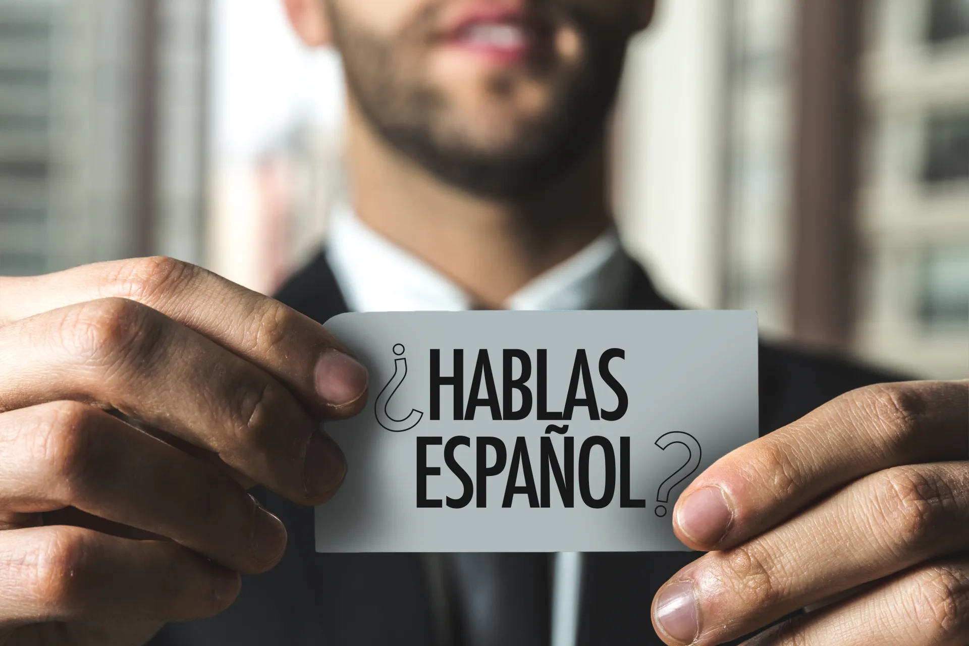 Ein Mann im Anzug, der ein Schild mit der Aufschrift &bdquo;&iquest;Hablas espa&ntilde;ol?&ldquo; in der Hand h&auml;lt.