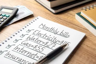 Notebook listing monthly bills for electricity, water, gas and internet next to a calculator and cash