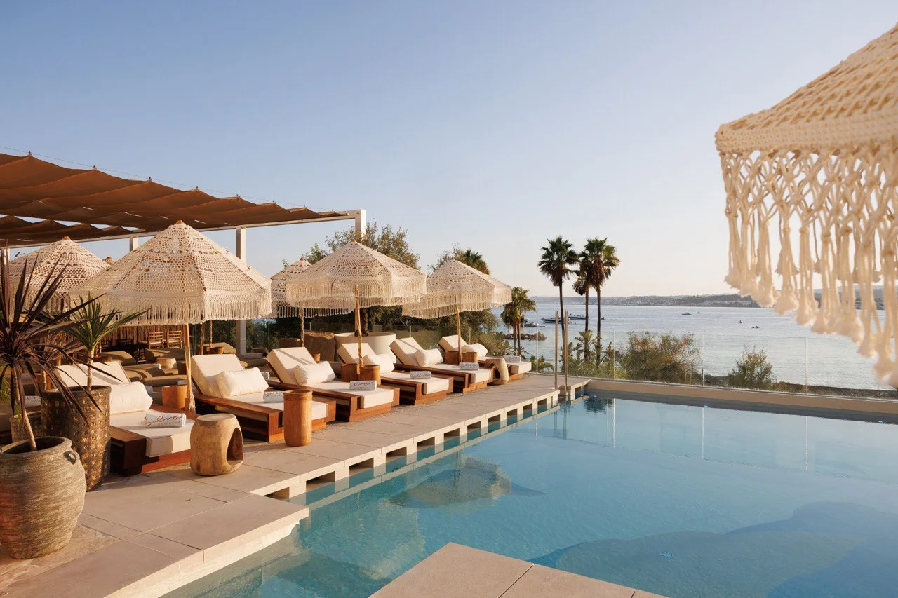 Sun beds and fringed umbrellas around the pool at Nube Estepona with the sea behind