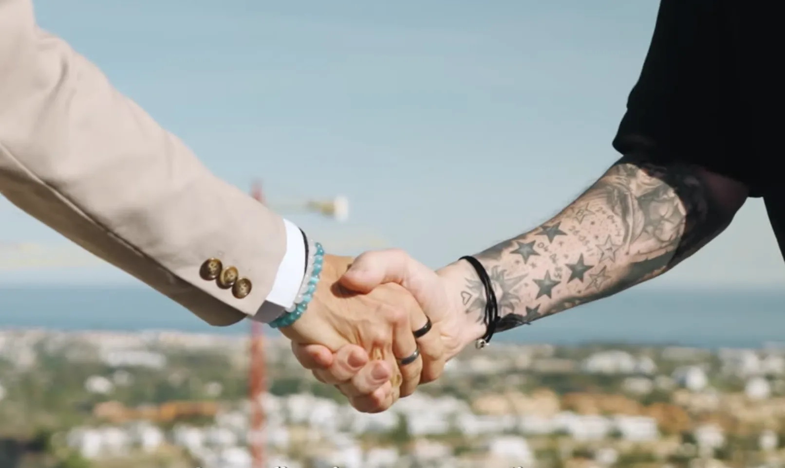Two people shaking hands above a hillside of white villas overlooking the sea
