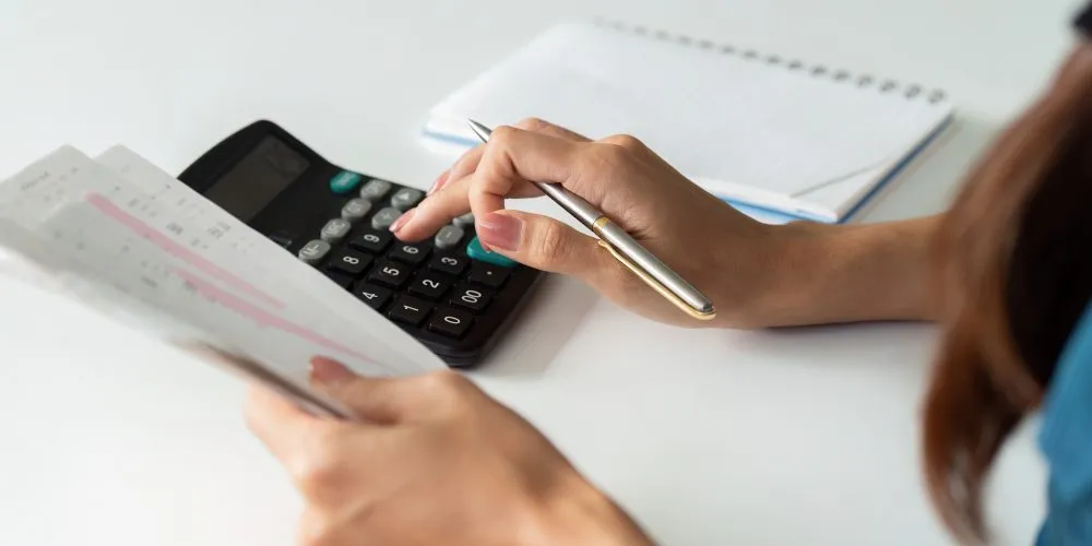 Woman calculating household bills with a calculator, pen and notepad